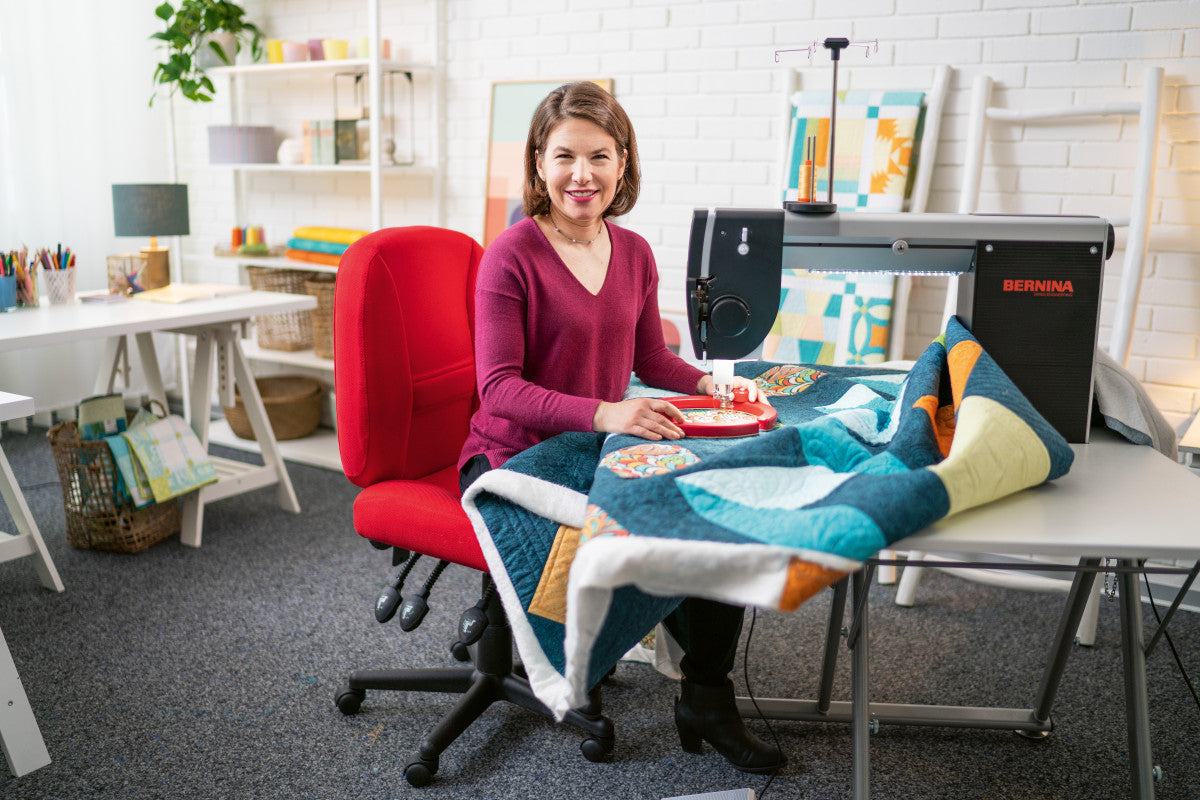BERNINA Q16 sit-down longarm in use by Amanda Murphy on a folding table with a quilt; shown accessories are illustrative